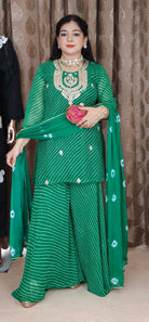 Woman in a green traditional outfit with jewelry against a patterned curtain background