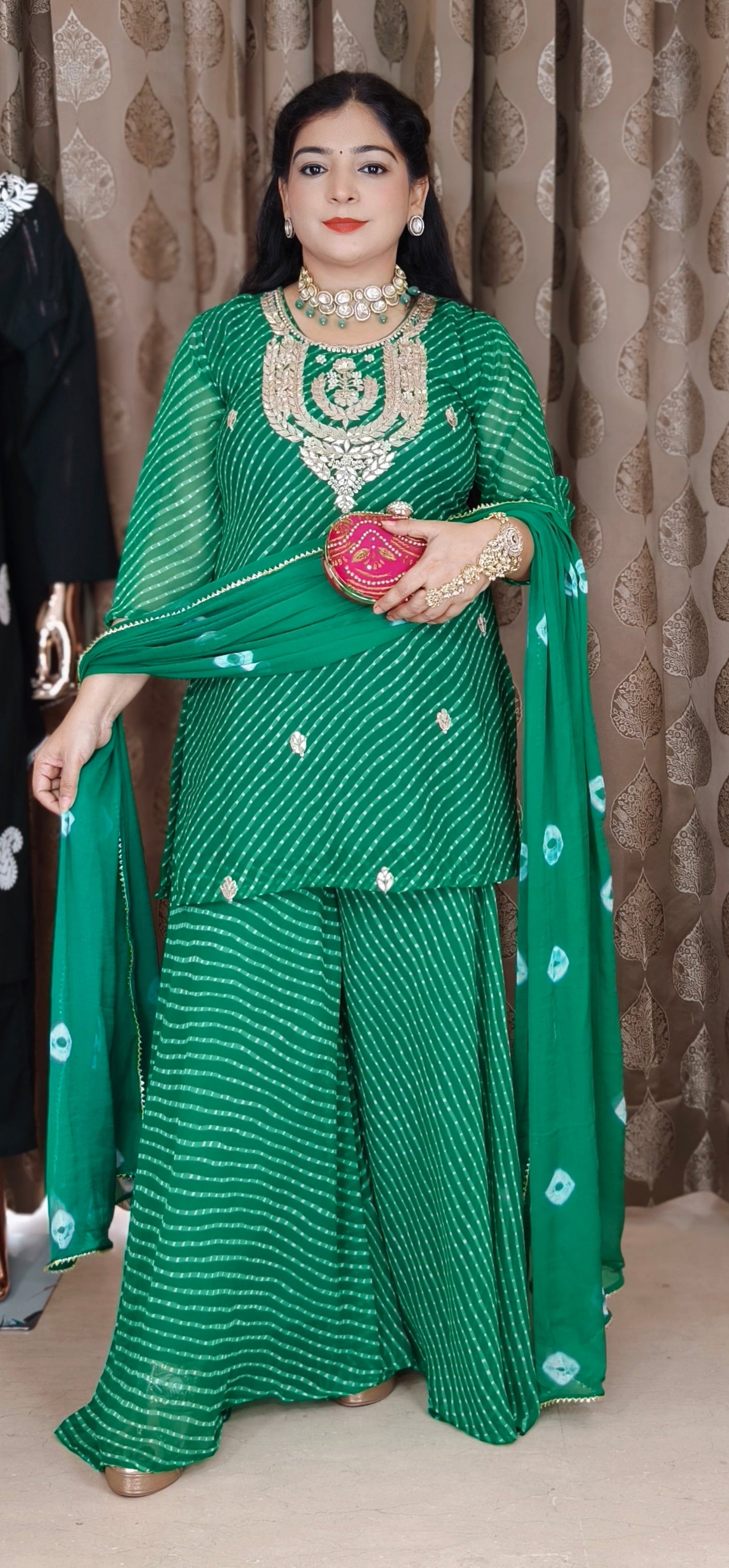Woman in a green traditional outfit with jewelry against a patterned curtain background