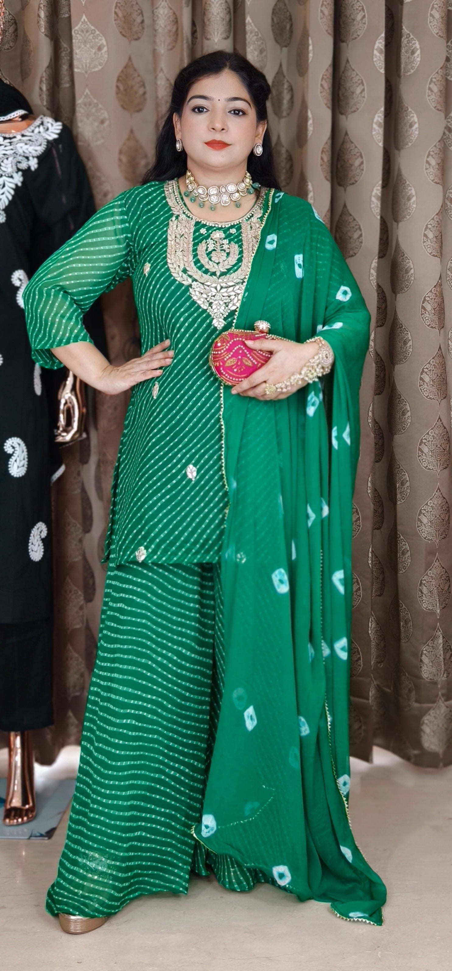 Woman in a green traditional outfit holding a red heart-shaped object against a patterned curtain background.