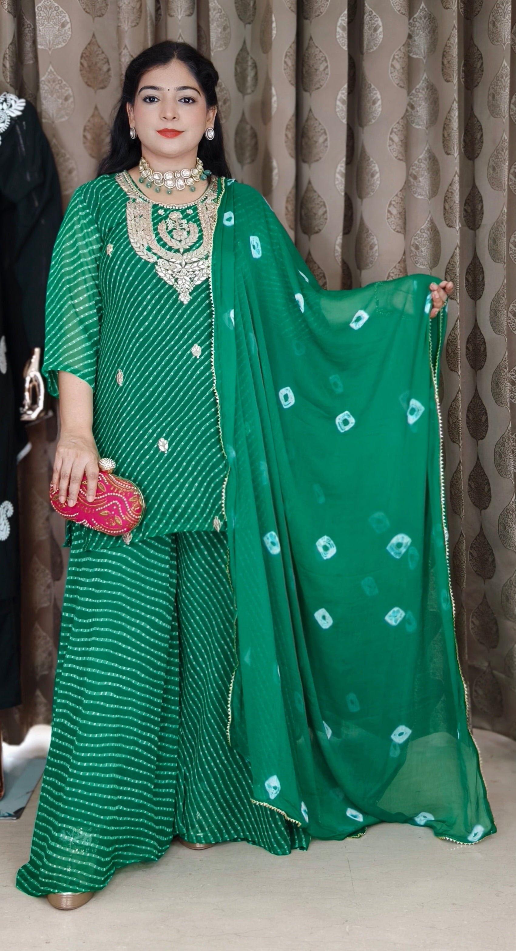 Woman in a green traditional outfit with white patterns against a textured wall.